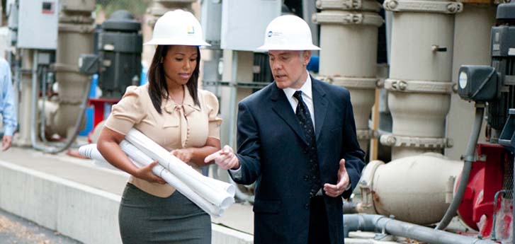 Male and female on site at a power plant wearing white construction hats