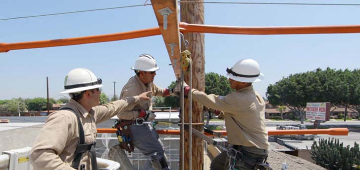 Three SCE service men in hard hats fixing a pole