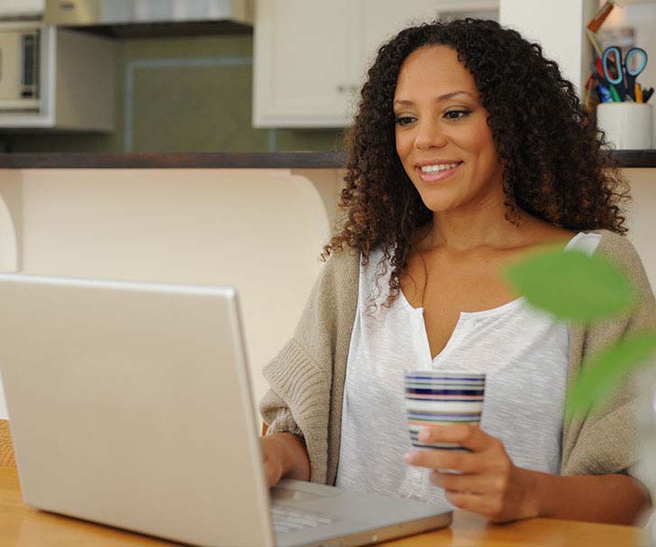 Woman holding a cup of coffee, while using a laptop