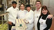 Four Homemade Baby employees in a commercial kitchen standing next to boxes of fresh produce